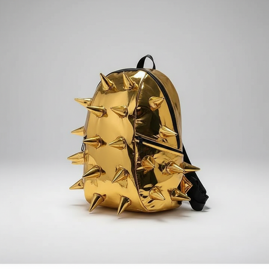 A metallic gold backpack with sharp, raised spikes, styled on top of a black book on gray steps.