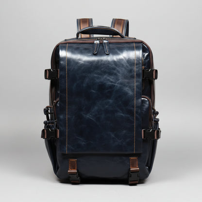 A dark navy blue distressed leather backpack with brown leather accents, zippers, and straps, shown from the back on a wooden surface against a textured brown background.