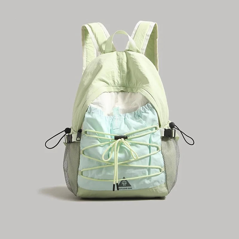 A light green and pale blue backpack with a drawstring front and mesh side pockets, shown against a solid gray background.
