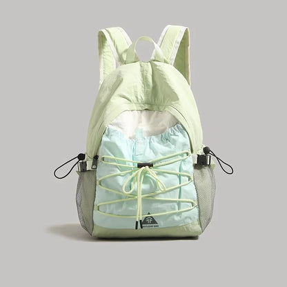 A light green and pale blue backpack with a drawstring front and mesh side pockets, shown against a solid gray background.