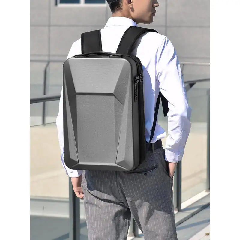 A man wearing a white dress shirt and gray pinstripe trousers is shown from the back, wearing a modern gray and black geometric laptop backpack.