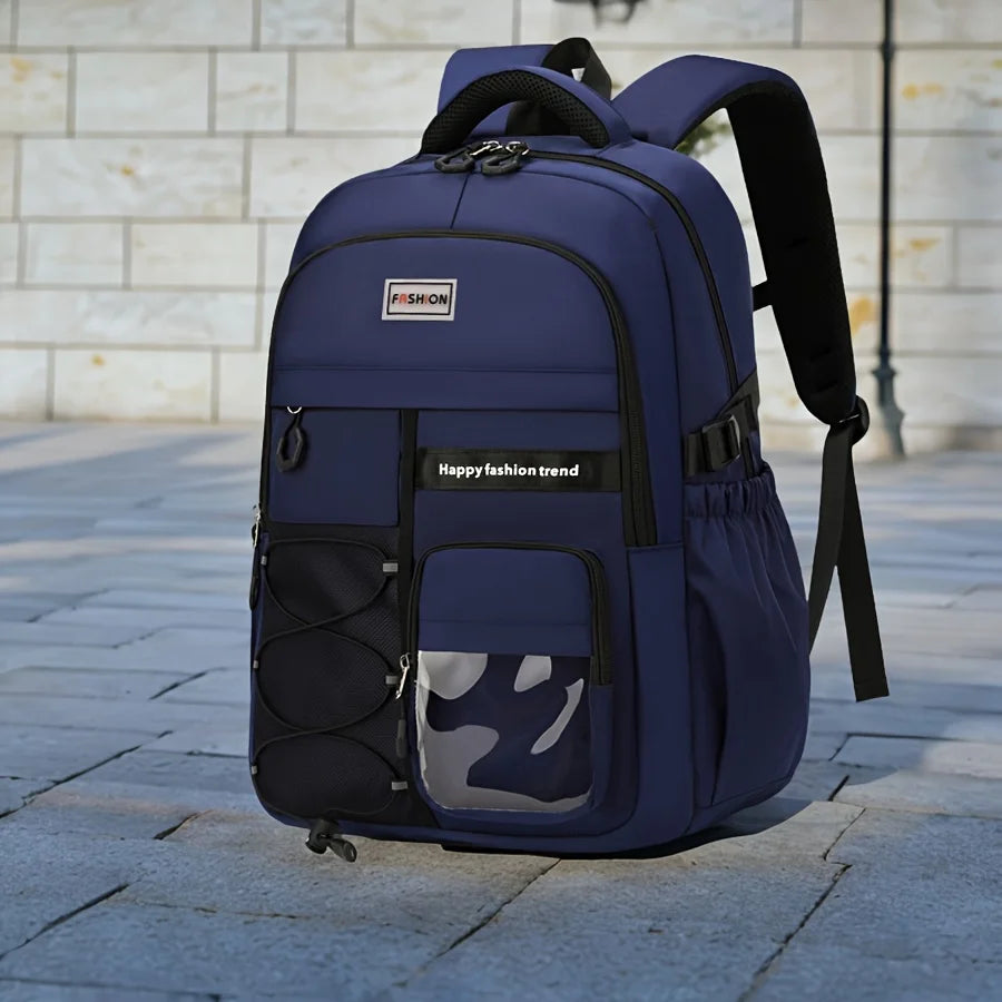 A navy blue backpack with black straps and trim, featuring a front zippered pocket with a gray and black camouflage mesh window, set on a paved stone surface against a light stone wall background.