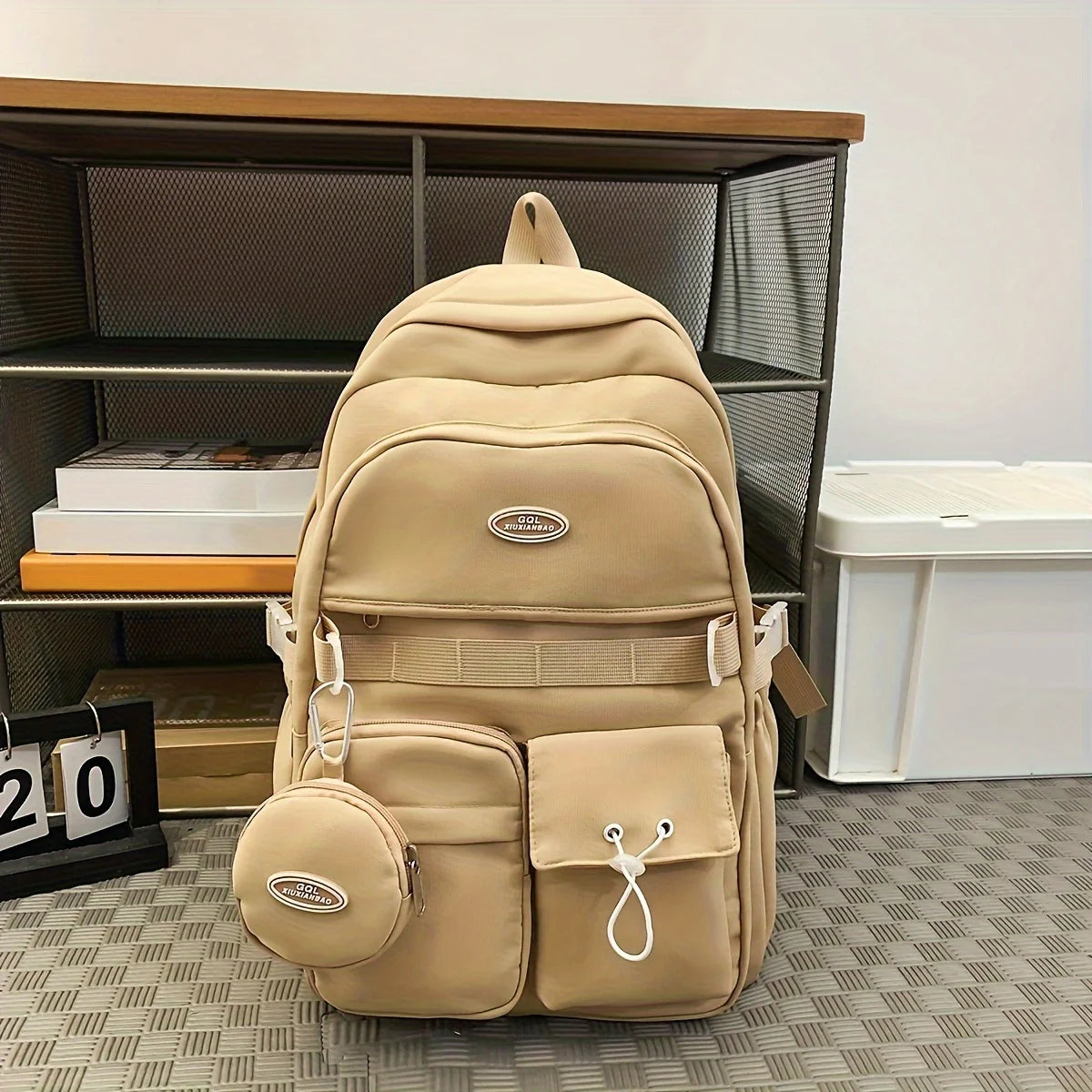Beige backpack with a small round pouch on a checkered floor.