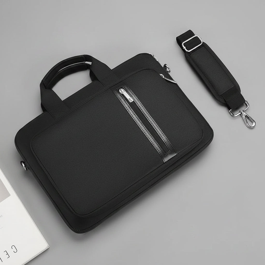 Black laptop bag with handle and shoulder strap on a gray surface with a laptop and mouse.