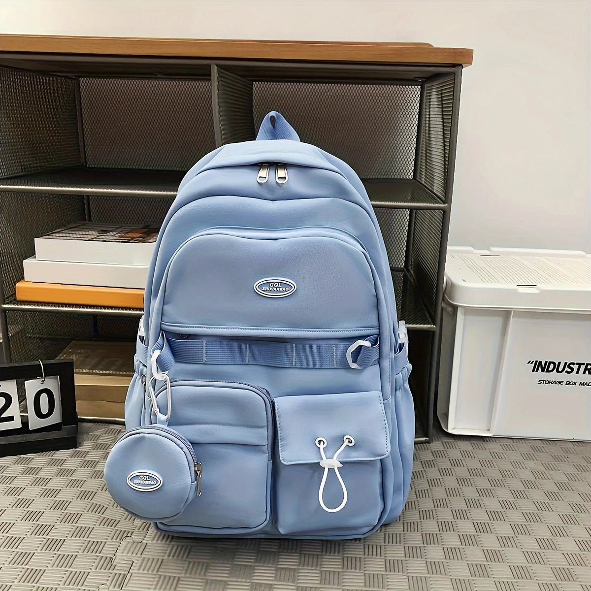 Blue backpack with a brand logo on a patterned floor next to a bookshelf.