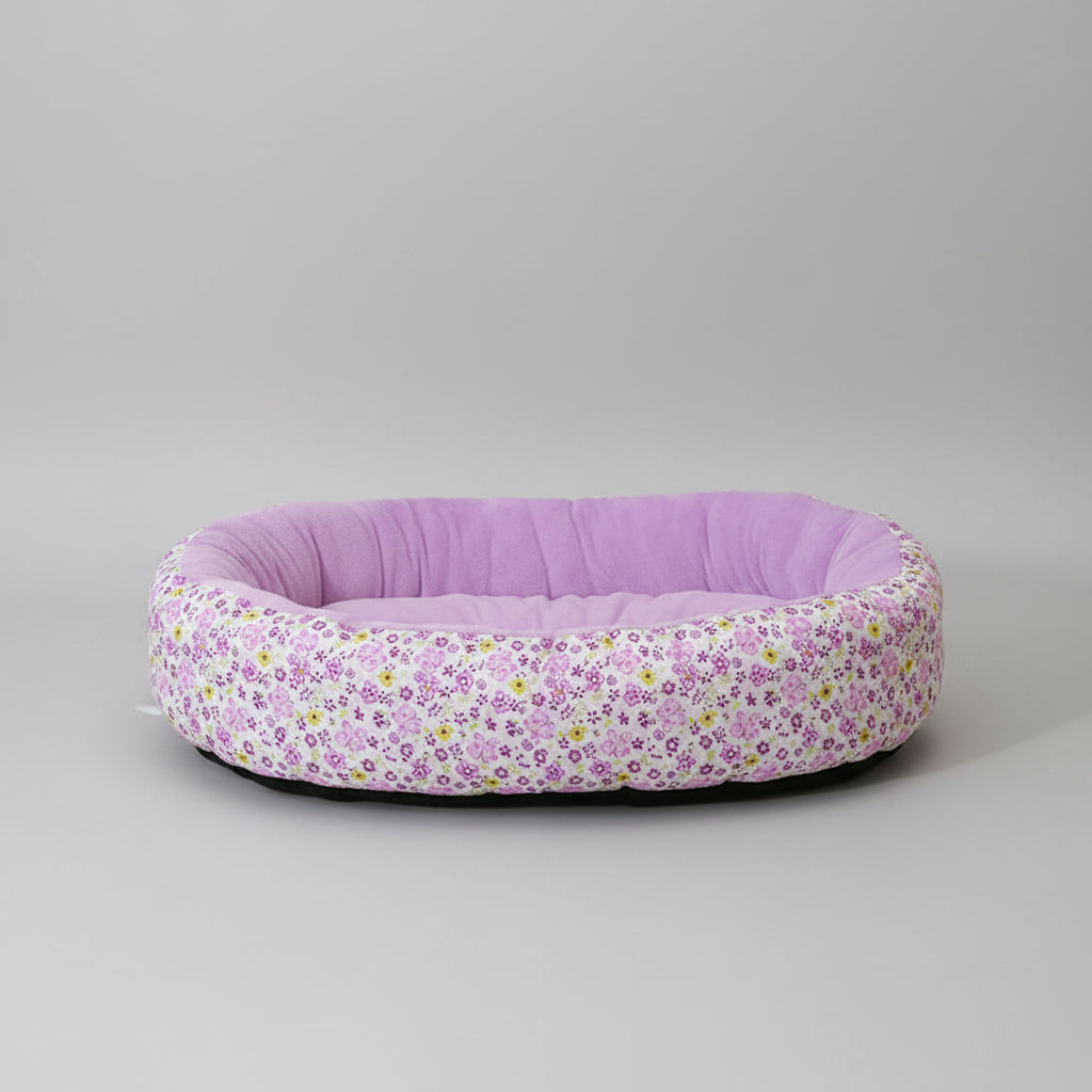 Floral-patterned pet bed with a solid purple interior on a pink surface.