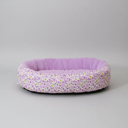 Floral-patterned pet bed with a solid purple interior on a pink surface.