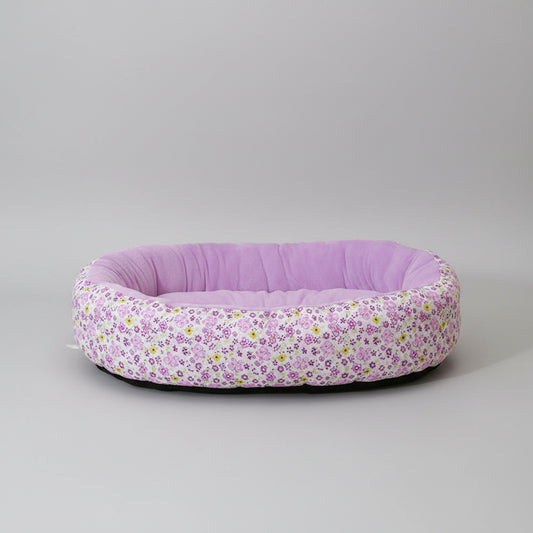 Floral-patterned pet bed with a solid purple interior on a pink surface.