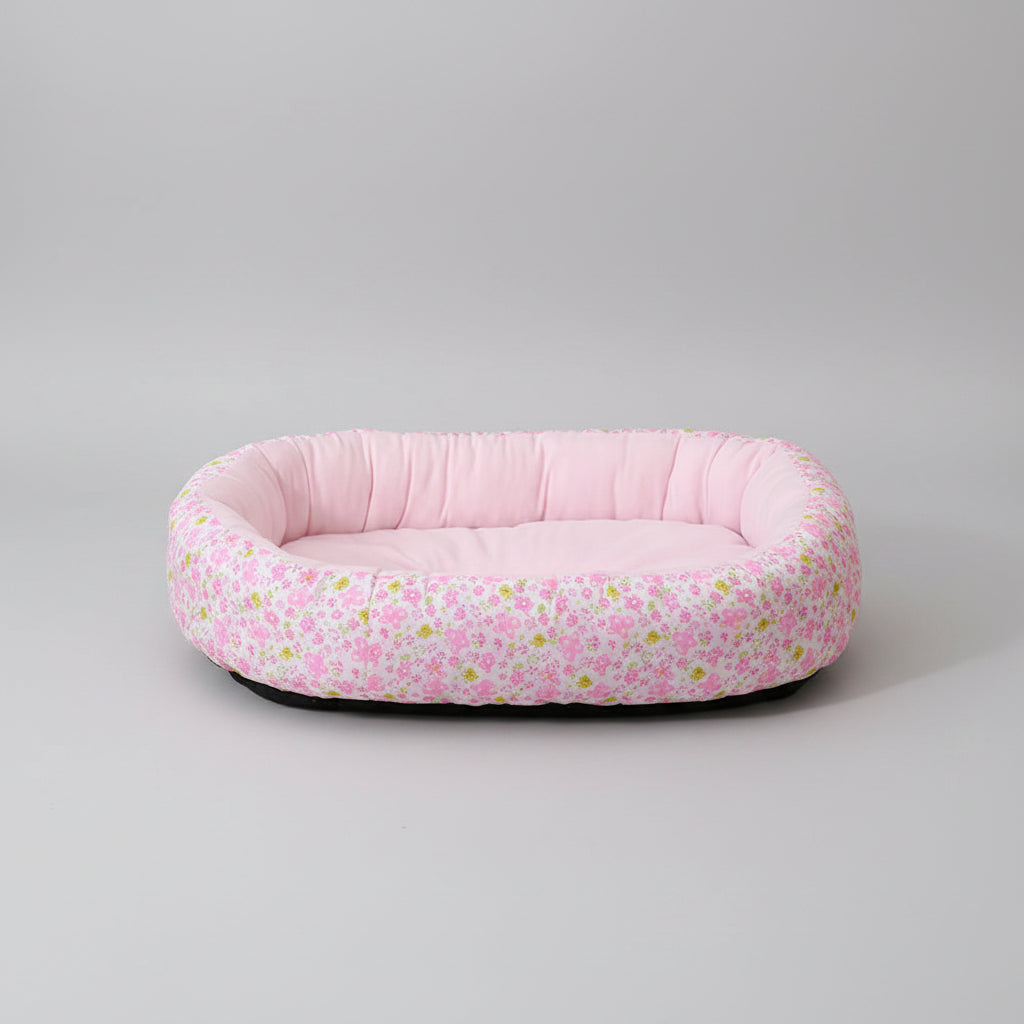 Floral patterned pet bed on a pink surface with a light curtain background
