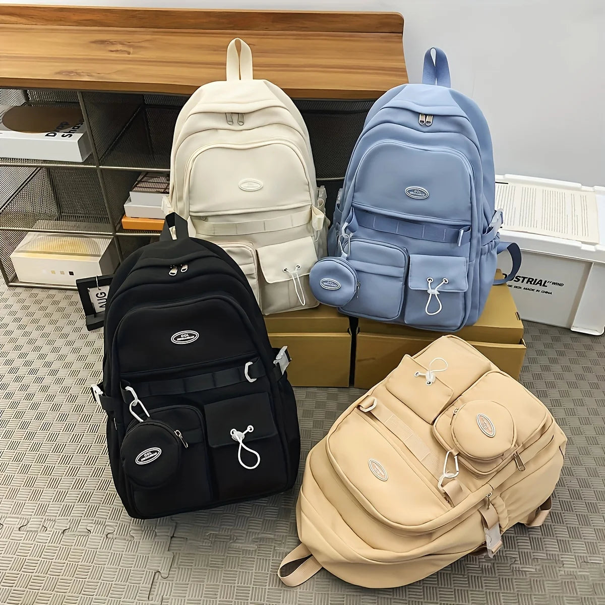 Four backpacks in black, beige, blue, and cream on a patterned floor.